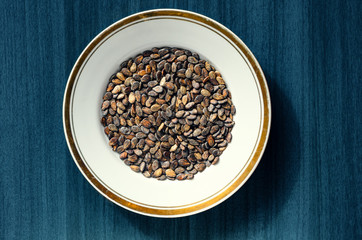 Watermelon seed kernels in a white round dish with a gold borders  on wood deep blue background