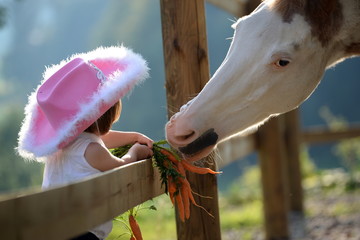 bribery, cute little cowgirl feeding a painthorse with carrots