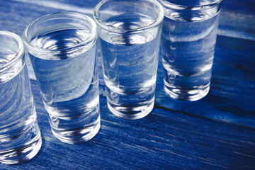 Vodka shots filled with alcohol on wooden blue bar.