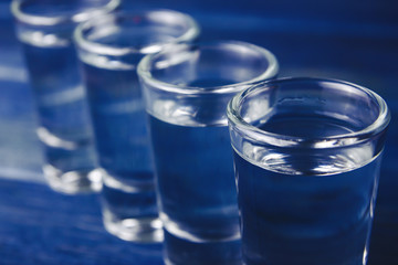 Shot glass filled with vodka on wooden blue bar.