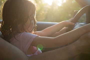 Petite fille apprenant à conduire sur les genoux de son père