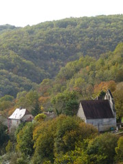 Fototapeta na wymiar Chapel and house nestling in a wooded valley in the Dordogne region of France with the foliage of the scrub oak starting to take on autumn colouring
