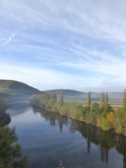 Early morning shot over a bend in the Dordogne river, near La Cave, Dordogne, France, in autumn with trees and clouds reflected in the still waters of the river and mist lingering above the water