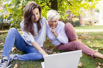 Fototapeta premium pretty mom and daughter consult the laptop under a tree in autum