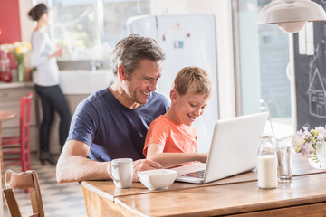  Cheerful father and son using a laptop while having breakfast