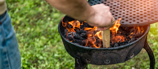Man on a lawn putting firewood into barbecue