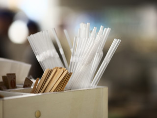 Plastic transparent straws, wooden sticks for coffee and drinks, and sugar over blurred background