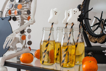 Glass bottles with apple juice, paper straws, ghost shaped marshmallow. A decorative Halloween mirror and  clementines. 