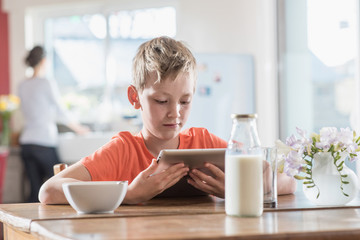A young boy using a digital tablet while taking his breakfast