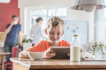 A young boy using a digital tablet while taking his breakfast