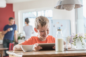 A young boy using a digital tablet while taking his breakfast