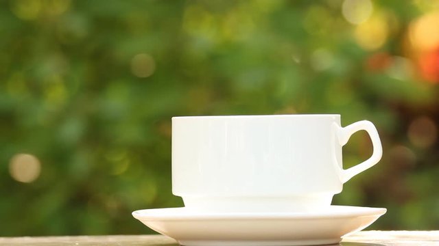 Hot cup of coffee on table with green leaves bokeh background
