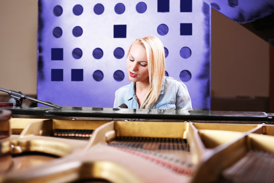 Young woman playing piano and singing in recording studio