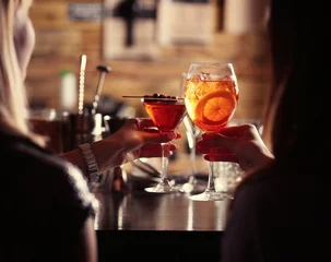 Rolgordijnen Vrouwen roosteren met cocktails in bar © Africa Studio