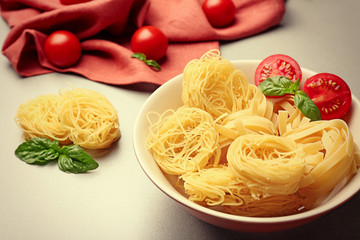 Bowl with pasta nests and cherry tomatoes on table, close up