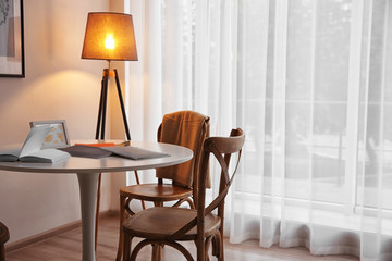Modern white table, floor lamp and wooden chairs near window