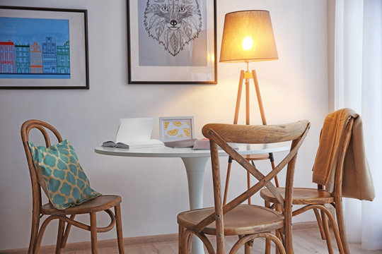 Modern white table, floor lamp and wooden chairs near wall