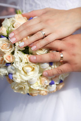 Obraz na płótnie Canvas Close up hands of bride and groom with wedding bouquet and golden rings