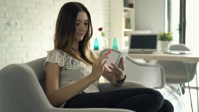 Young, pretty woman using smartphone sitting on sofa at home
