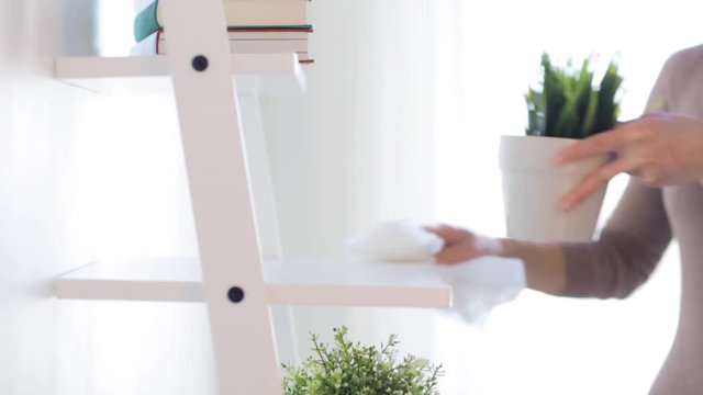 woman with duster cleaning shelf from dust at home