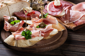 Spanish tapas with slices jamon serrano, salami, olives and cheese cubes on a wooden table