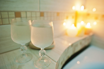 Two wet glasses of wine background burning candles in bathroom