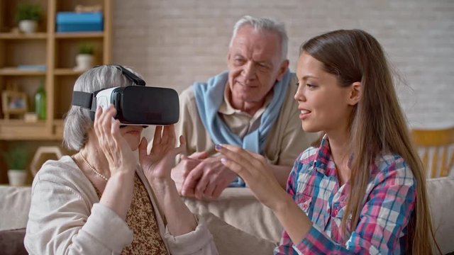 Young woman sitting beside grandmother in virtual reality headset and explaining how it works
