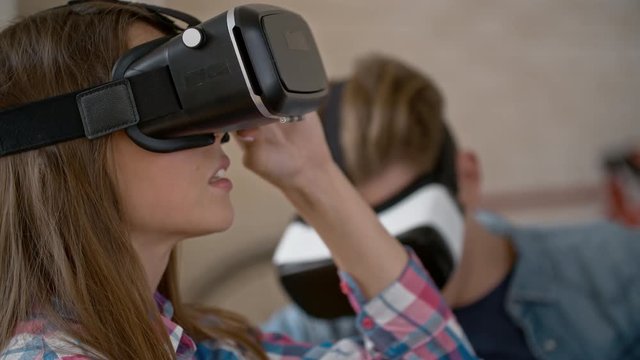 Rack focus from laughing young man in virtual reality headset looking around room to young woman wearing VR goggles and smiling