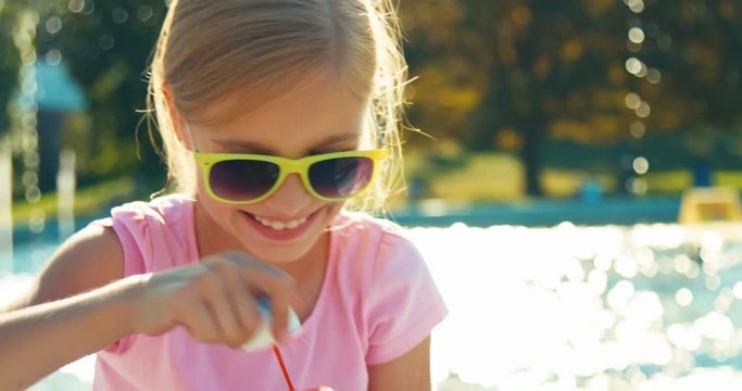 Close Up Portrait Laughing Child Girl 7-8 Years In Sunglasses Blowing Soap Bubbles On Fountain Background At Sunny Day