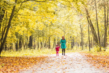 Fototapeta premium Mother and daughter walking holding hands at park. Family lifestyle, autumn season concept