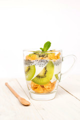 Delicious and healthy yogurt parfait made with homemade yogurt, kiwi fruit, corn flakes and sweet basil seeds with wooden spoon on wooden background; healthy dietary start eating good food.