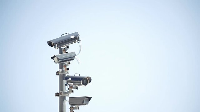 Many surveillance cams on a pole, watching the neighbors. Harsh colors, slow zoom in movement.
