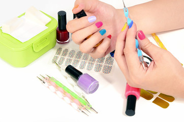 Obraz na płótnie Canvas Woman hands doing rainbow manicure.Table full of manicure ustensils,coloured nail polish,nail decals stickers,striping tape,nail file,dotting pens,vinyl sheets.Nail art accesories isolated on white. 
