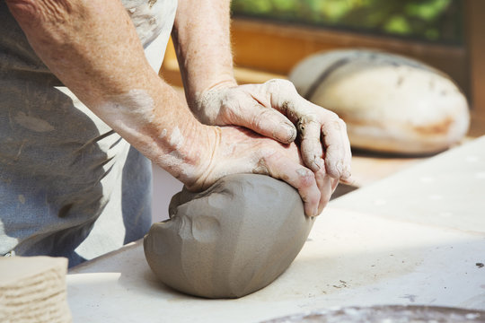 A person, potter preparing a lump of damp clay for throwing. 