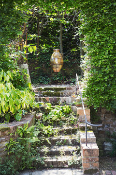 A glazed or amphora in a frame on a terrace at the top of steps, under a pergola. 