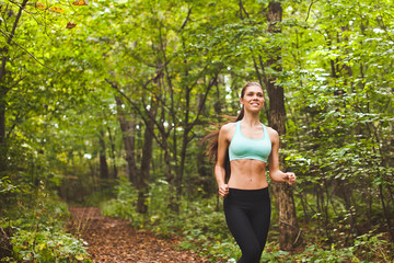 Attractive woman athlete running on path in green summer forest