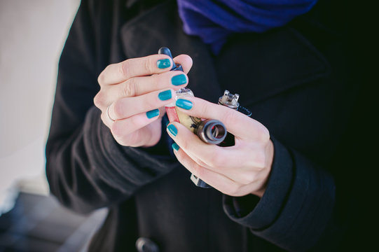 portrait of young beautiful woman with white hair, in a black coat, a skirt and a black hat, smoking an electronic cigarette, runs vape juice electronic cigarette. He holds a mechanical mod with RDA. 