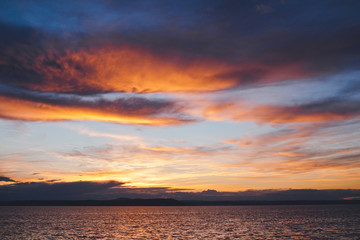 Obraz premium Bright coloured sunset behind clouds and island in ocean