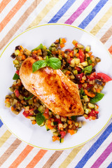 Fried chicken breast with sauteed vegetables: eggplant, carrot, zucchini, squash and tomatoes. View from above, top studio shot
