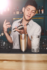 Young handsome barman pouring cocktail drink into glass