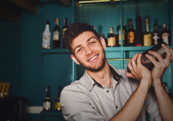 Young handsome barman in bar shaking and mixing alcohol cocktail