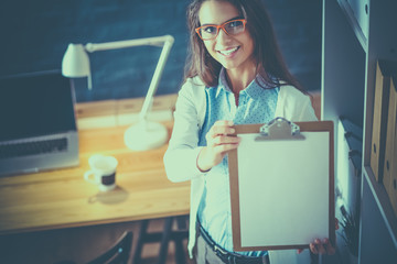 Young woman standing near desk with laptop holding folder