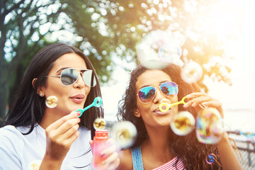 Female friends with sunglasses blow bubbles