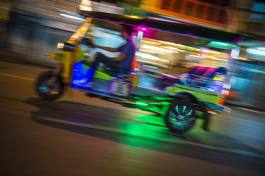 Bangkok Thailand tuk-tuk taxi zooms by in a brightly colored lights night blur