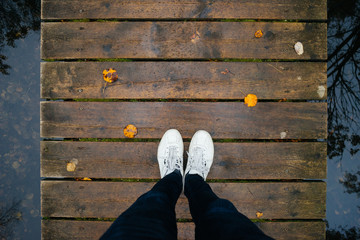 Male legs in sneakers on wooden bridge by autumn
