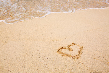 Heart symbol on the sand and sea wave.