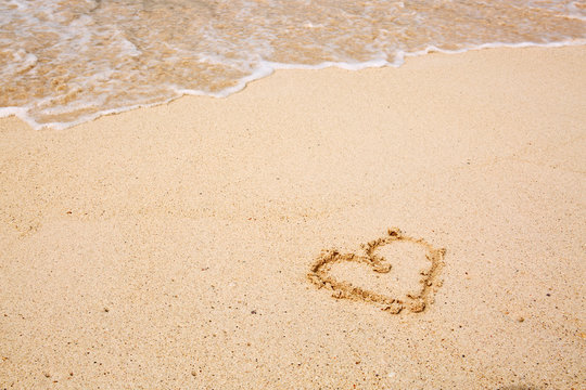 Heart symbol on the sand and sea wave.