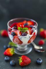 Yogurt with fresh berries fruit and chia seeds on stone background.