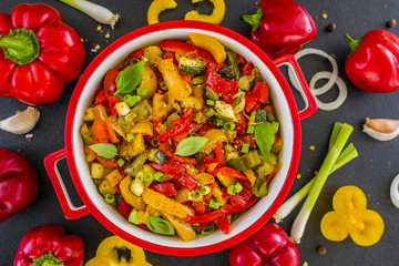 Delicious stewed colored peppers with onions, herbs and spices on dark stone background. vegetarian food. Healthy diet.