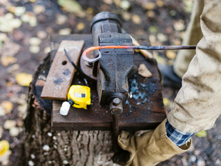 Blacksmith holds curved hot red iron rod in vise